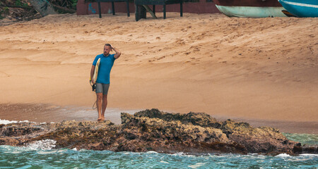 Mężczyzna surfer idący z deską surfingową tropikalną plażą.