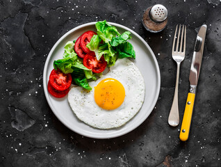 Breakfast plate - fried egg, bacon and vegetables salad on a dark background, top view