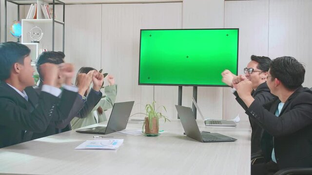 Young Asian Team Have Meeting In A Conference Room, Have Conference Video Call Tv Mock Up Green Screen,  They'Re Happy And Celebrate With High Five And Cheers
