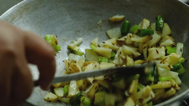 A female hand stirring the frying vegetables in a pan