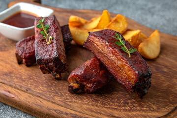 Grilled pork ribs plate with fried potatoes and barbecue sauce. Ready menu for the restaurant. Neutral gray blue textured background