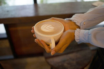 Hand put a Latte arts coffe hot coffee on wooden table.barista love art concept.