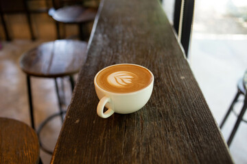 Hand put a Latte arts coffe hot coffee on wooden table.barista love art concept.