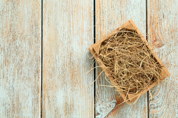Dried hay in crate on light wooden background, top view. Space for text