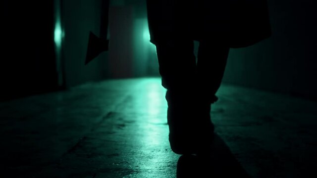 Maniac walking with axe in dark corridor. Mystical scary murderer going to kill, carrying murderous weapon. Halloween costume of killer. Horror scene or nightmare concept. 