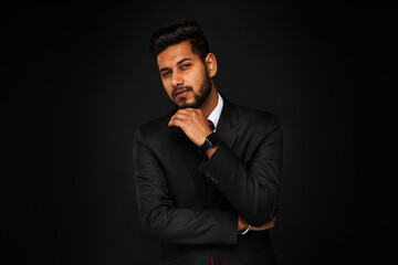 Portrait of young stylish bearded indian business man in black suit on black isolated background