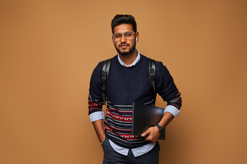 Handsome indian manager with laptop and backpack on studio background