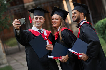 Group of international graduates in graduation gowns make selfie in campus