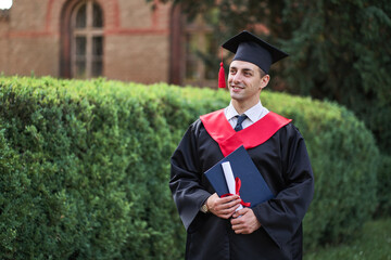 Smiling caucasian male graduate student in graduation robe with iploma