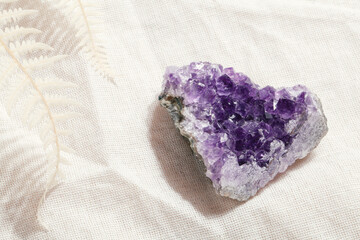 druse raw purple amethyst crystal on piece of stone on grey linen with fern