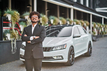 Tall Indian businessman near a car in a suit