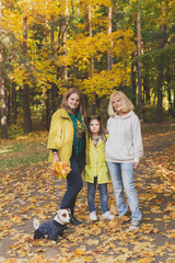 Naklejka na ściany i meble Portrait of three generations of happy beautiful woman and dog looking at camera, hugging and smiling in autumn nature.