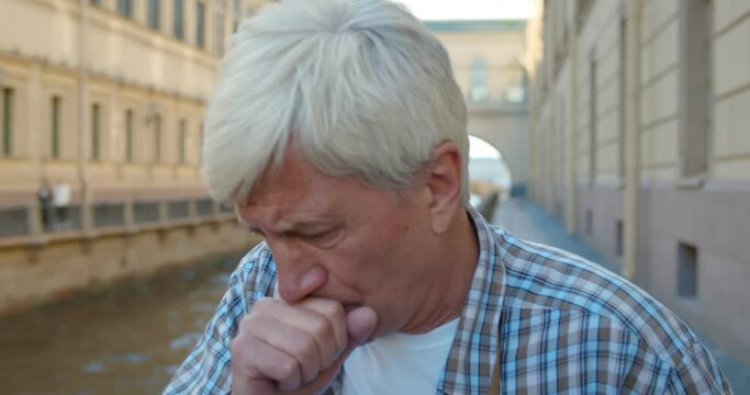 Close up portrait of senior man feeling unwell and coughing outdoors