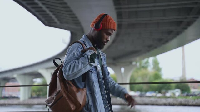 Handsome guy listening to music in headphones and dancing while walking in city spbas. Close-up view of American African man listens to song and moves his body, looks with happy smile and walks