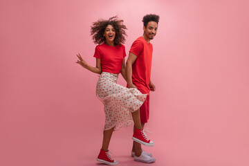 Funny young hispanic couple jumping and smiling on isolated pink background. Man and woman in dark...