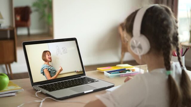 Child listening to teacher on laptop screen and learning while sitting at table at home spbas spbd. Close view of Caucasian schoolgirl looks at computer monitor and listens, female teaches and works