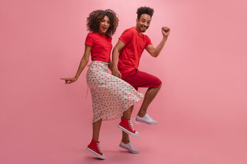 Young african woman and man jumping hand in hand having fun with copy space. Best friends, dressed in T-shirt and sneakers, look stylish and bright together. Emotions of people and fashion concept.