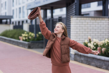 Fototapeta premium A dream come true. Cute caucasian girl in a brown beret and brown clothes shouts cheers while gesturing with her hand on a city street