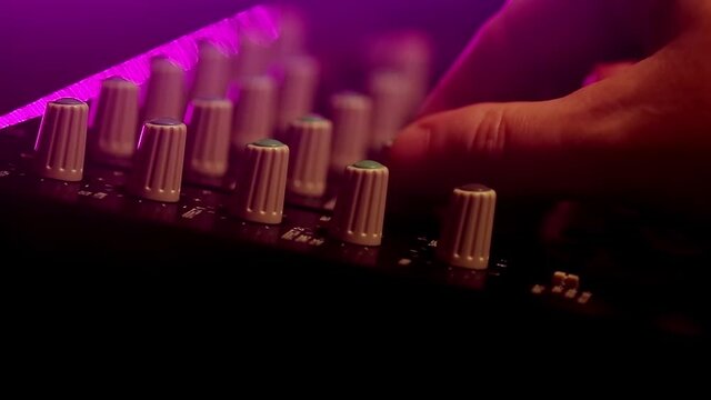 Portative cassette tape studio mixer with hand adjusting knobs. Closeup shot in neon light.