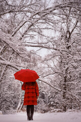 A happy woman walks with a red umbrella in her hands, a winter park with snow-covered trees