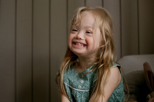Portrait of little girl with Down Syndrome sitting on chair and laughing