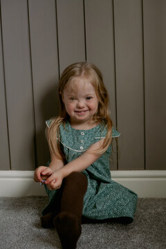 Portrait of little girl with Down Syndrome sitting on floor and laughing