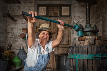 Grape harvest: Old woman smiling winemaker  working on a traditional winepress for the must pressing. Old winery background
