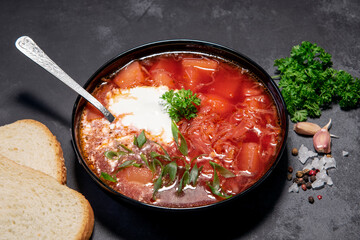 Borsch. Ukrainian soup. Red soup. Borsch with sour cream and onions, white bread. Traditional Russian borsch with sour cream. The concept of delicious food with sour cream on a black background
