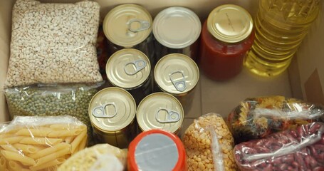 Young Asia teenage girl volunteer wear gloves packing food and drinks donation into donations paper boxes while working in charitable foundation. Social worker, food bank and coronavirus concept.