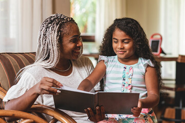 Madre e hija latinas compartiendo tiempo en casa mientras leen un libro juntas