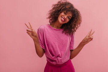 Medium-sized image of sincere young Afro woman with open bright smile and style on pink background....