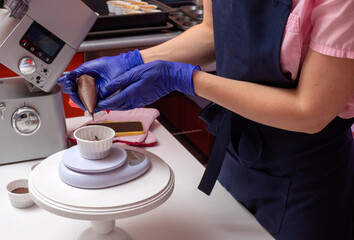 The pastry chef squeezes the chocolate dough out of the pastry bag with his hands into a cupcake mold, which stands on the kitchen scales. The cooking process, the division into portions.