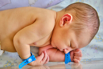 A newborn baby with a maternity hospital bracelet on his arm is sleeping in a crib. A newly born child in a clinic bed behind a transparent glass