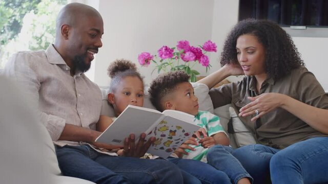 Parents reading book with children sitting on sofa in lounge at home - shot in slow motion