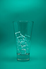 Ice cubes in empty glass, long glass on green background, front view with details