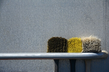 Three scrubbing brushes on holder beside metal boat siding.