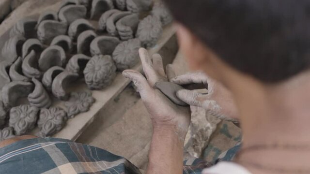 Unrecognized Poor Asian man making idols and sculpture with clay, slow motion over the shoulder shot