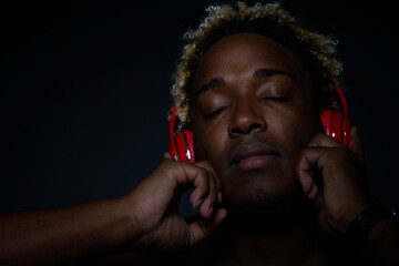 Black man in red wireless headphones listens to music and enjoys music on a black background