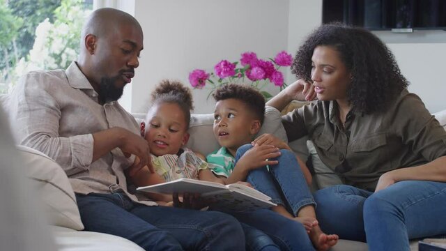 Parents reading book with children sitting on sofa in lounge at home - shot in slow motion