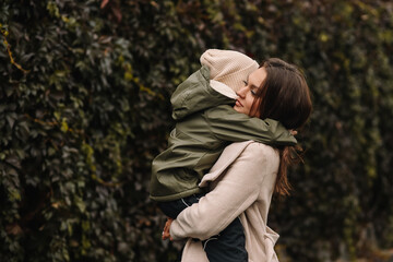 Fototapeta premium Happy cheerful mother and a small child son in warm clothes walking among plants in an autumn park in nature in fall outdoor, selective focus