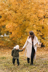 Happy cheerful mother and a small child son in warm clothes walking among plants in an autumn park in nature in fall outdoor, selective focus