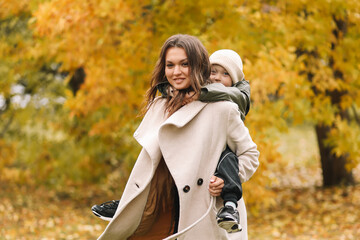 Happy cheerful mother and a small child son in warm clothes walking among plants in an autumn park in nature in fall outdoor, selective focus