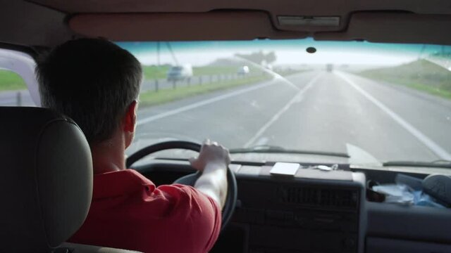 concentrated man with gray hair in red jersey drives minivan along highway and carefully look at road through windshield