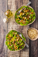 Delicious light dinner, lettuce with fried slices of zucchini, mango and shrimp and almond petals, water with lemon in a glass