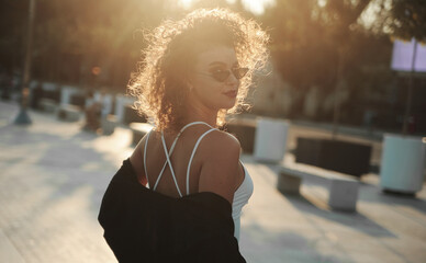 curly hair woman in sunglasses and leather jacket posing on dark background
