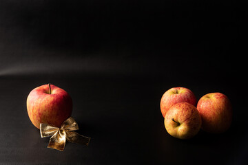 Apples, beautiful apples and a golden bow arranged over black background, Low Key portrait, selective focus.