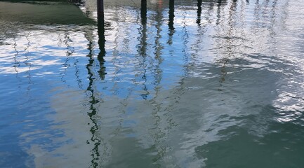 Water level reflecting the masts of sailboats, port moorings and blue sky with white clouds