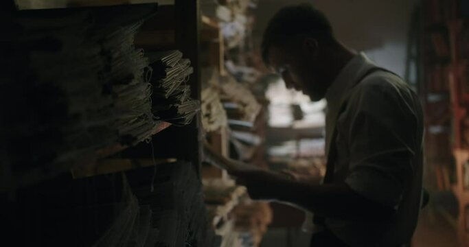 The secret of archival documents and a detective looking for information stands near a shelf with newspapers in a dark basement with documents from the Second World War
