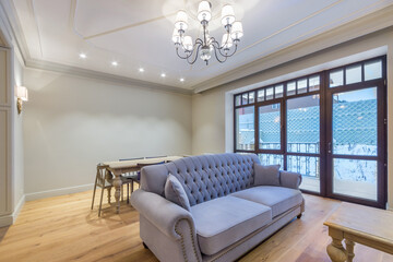 Fototapeta premium A modern living room in blue tones, with a panoramic window, a vintage chandelier, a sofa and a table. Interior of a cottage or townhouse