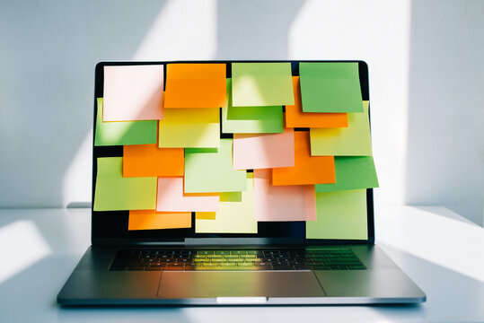 Workplace with laptop computer with many colorful empty sticky notes on display.